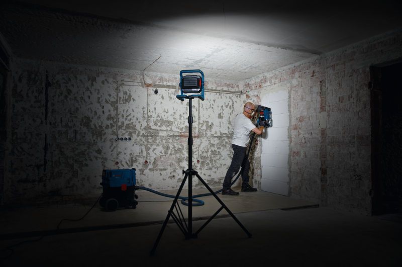 一名佩戴安全设备的人员在工作灯下操作墙壁钻孔工具。