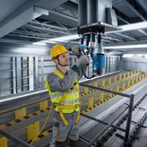 一名佩戴安全装备的人员正在操作磁力钻机钻削钢梁。