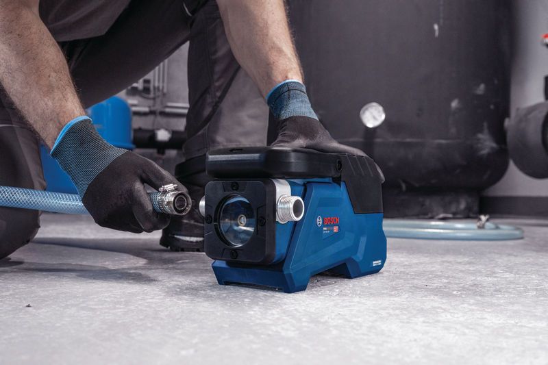 一名佩戴安全装备的人员将软管连接到一台小型蓝色水泵上。