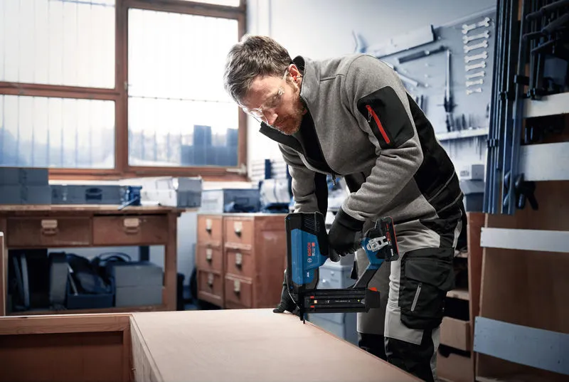 一名佩戴安全装备的人员正在使用无绳射钉枪安装木制家具。