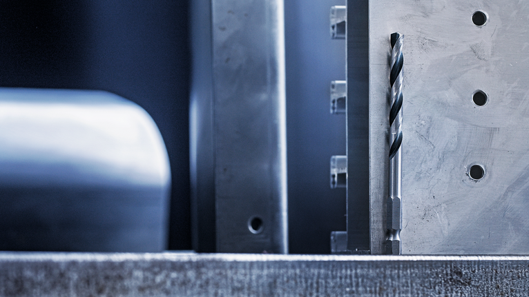 金属钻头垂直对准加工过的金属表面，该表面已钻孔。