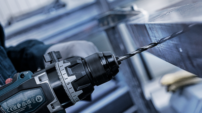 一名佩戴安全装备的人员在金属梁上钻孔。