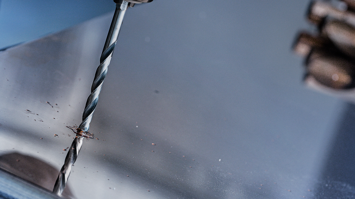 一名身穿安全装备的人员正在金属板上钻孔。