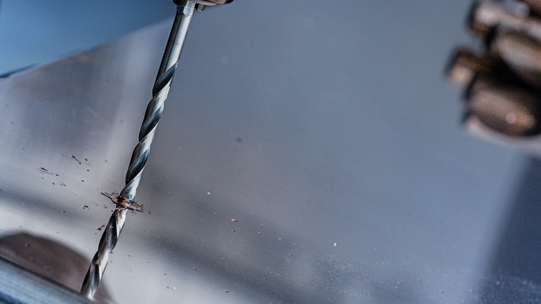 一名身穿安全装备的人员正在金属板上钻孔。