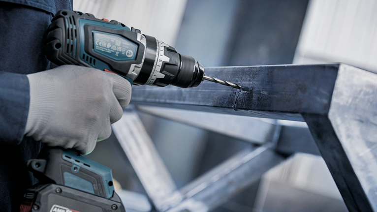 一名佩戴安全装备的人员正在金属框架上钻孔。