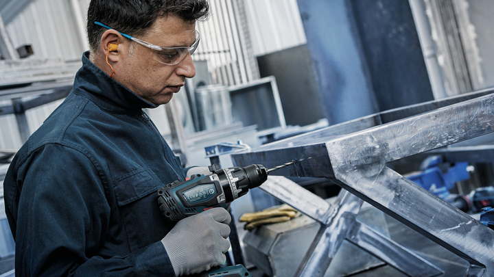 一名佩戴安全装备的人员正在金属框架上钻孔。