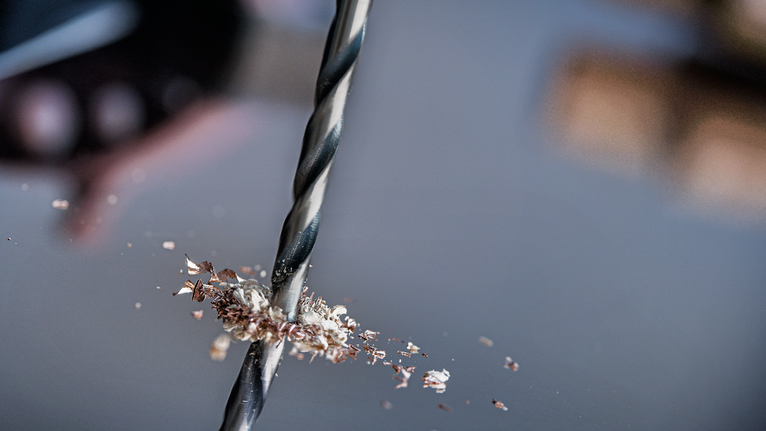 钻头在金属上钻孔，金属屑散落在周围。
