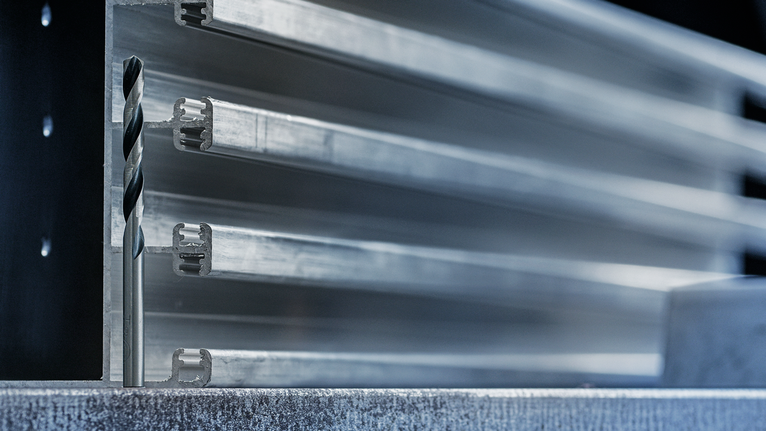 钻头竖直放置在堆叠金属型材前方的金属表面上。