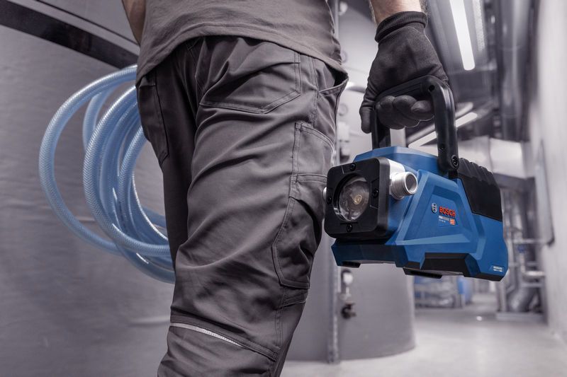 在工业环境中，一名身穿安全装备的人员携带一台蓝色便携式真空泵。