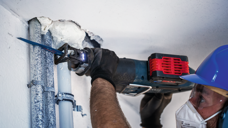 一名佩戴安全装备的人员使用往复锯切割管道。