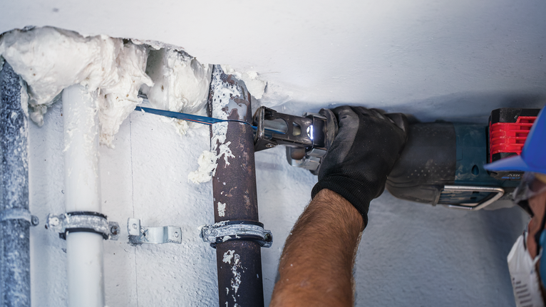 一名佩戴安全装备的人员使用电动工具切割金属管。