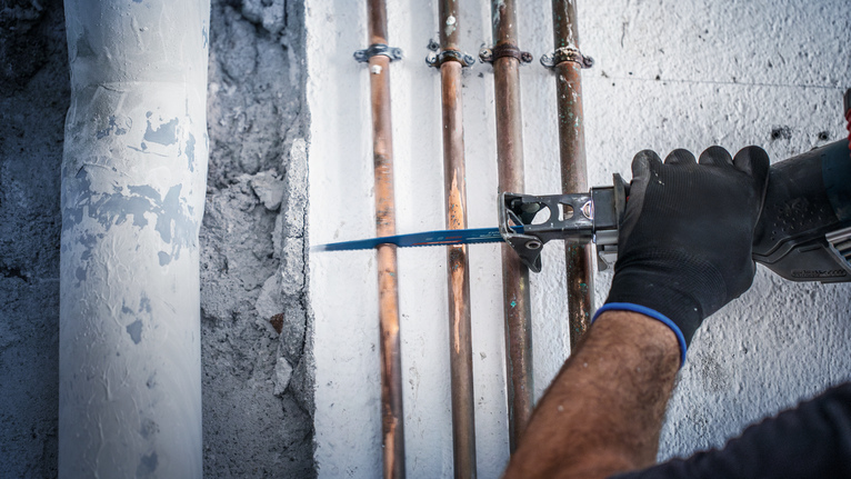 佩戴安全装备的人员使用往复锯在铜管附近进行切割。