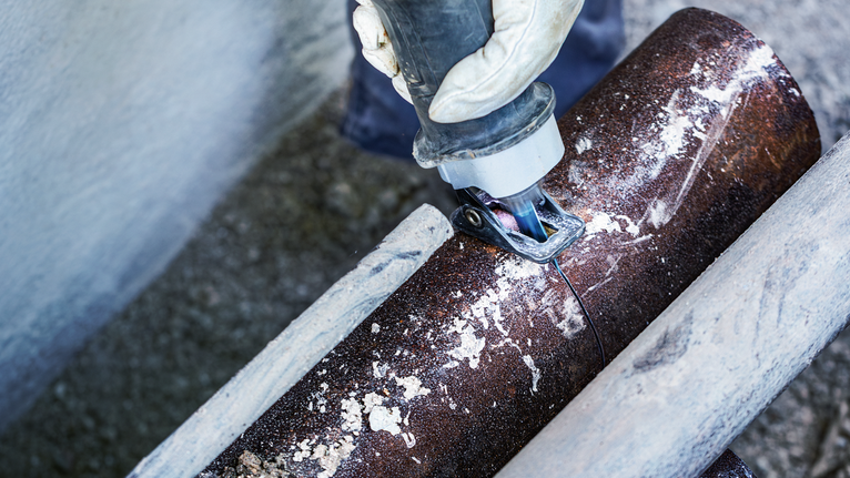 一名佩戴安全装备的人员使用电动工具切割金属管。