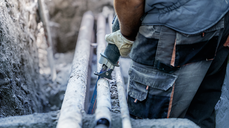 一名佩戴安全装备的人员使用往复锯切割管道。