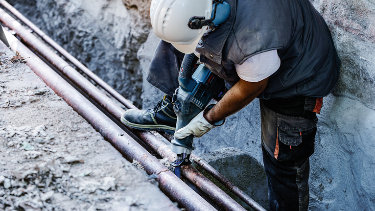一名佩戴安全装备的人员在建筑工地钻穿管道。
