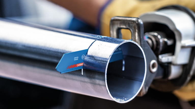 一名佩戴安全装备的人员用往复锯切割金属管。