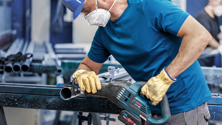 一名佩戴安全装备的人员正在用电动工具切割金属管。