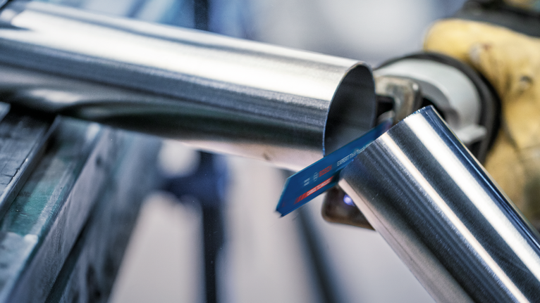 一名佩戴安全装备的人员正在用往复锯切割金属管。