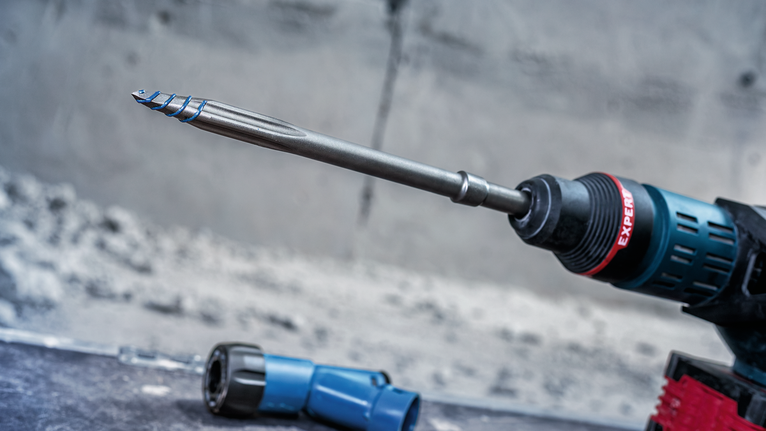 一台装有长钻头和蓝色工具部件的旋转冲击钻在混凝土表面上作业。