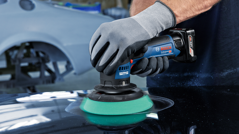 一名佩戴安全装备的人员使用手持式电动工具抛光汽车表面。