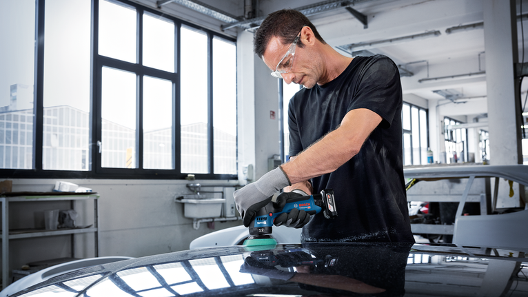 一名佩戴安全装备的人员使用无线电动工具打磨汽车表面。