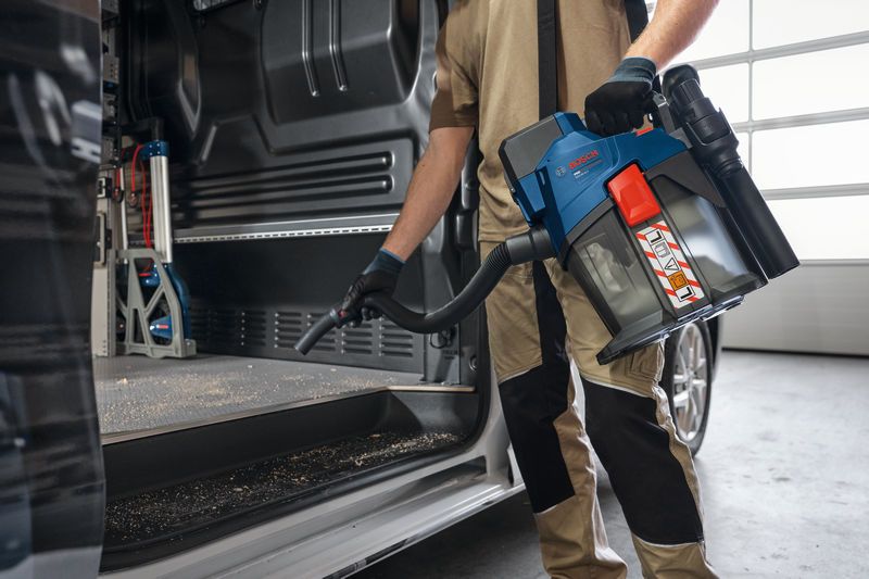 一名佩戴安全装备的人员使用无线吸尘器清洁车辆内部。