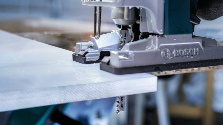 在车间里用曲线锯切割白色塑料板。