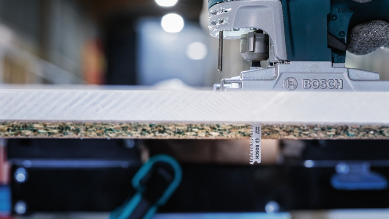 车间里，一把曲线锯正在切割一块层压木板。