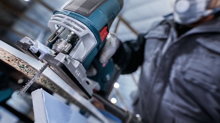 佩戴安全装备的人员使用曲线锯切割一块材料。