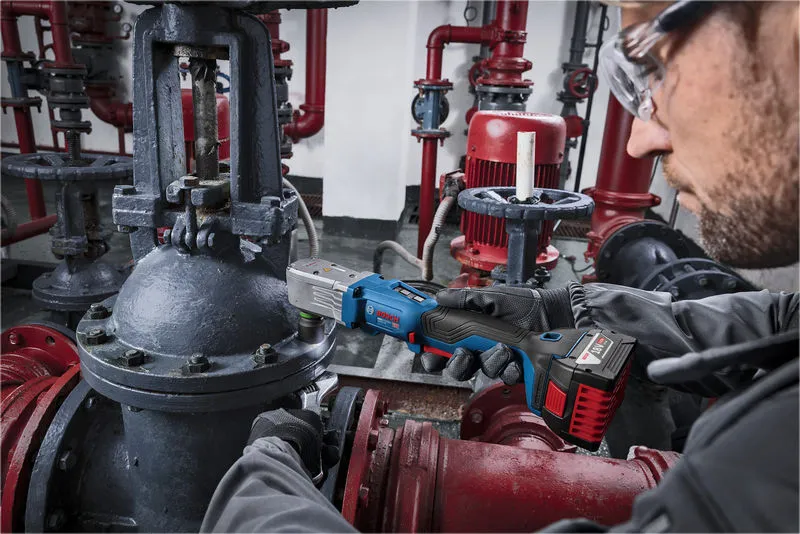 一名佩戴安全装备的人员正在使用无绳冲击扳手维修工业管道。