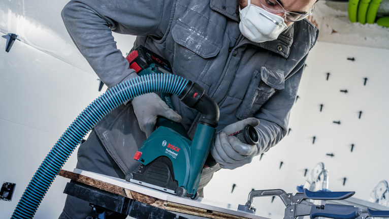 一名佩戴安全装备的人员使用带除尘功能的电锯切割木板。