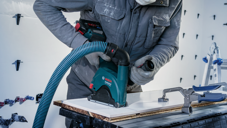 一名佩戴安全装备的人员正在使用带除尘功能的电动工具清洁瓷砖。