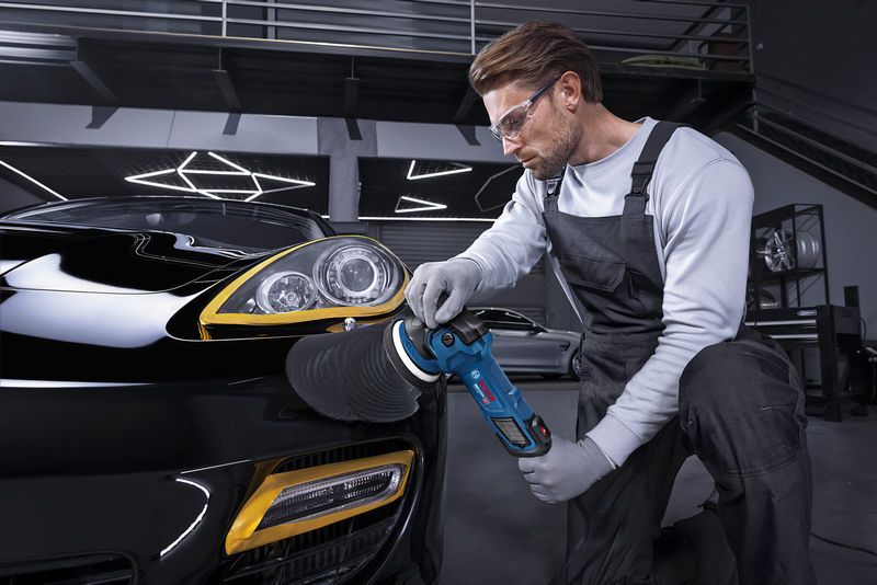 一名佩戴安全装备的人员正在用抛光工具擦拭一辆黑色汽车的前大灯。