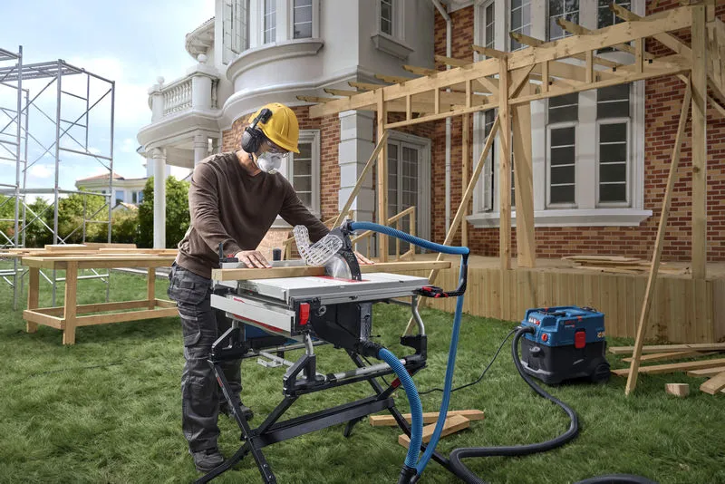 在房屋建筑工地，一名佩戴安全装备的工人正在用台锯切割木材。