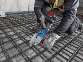 一名佩戴安全装备的人员使用无绳工具在建筑工地切割钢筋。