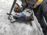 一名佩戴安全装备的人员在水泥地面上使用无绳钢筋切割机。