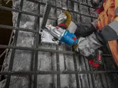 一名佩戴安全装备的人员使用无绳工具切割混凝土表面的钢筋。