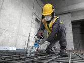 一名佩戴安全装备的工人正在使用无绳钢筋切割机切割钢筋。