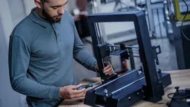 一个人在工作台上用螺丝刀组装3D打印机框架。