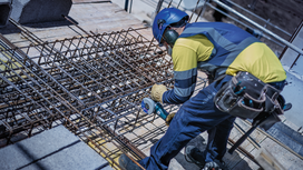 一名佩戴安全装备的人员在建筑工地使用电动工具切割钢筋。