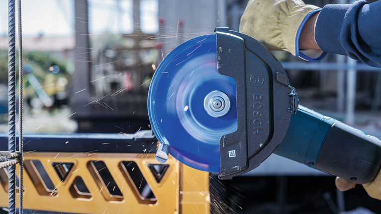 身穿安全装备的人员使用旋转式电动切割机切割金属棒。