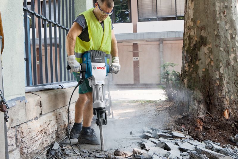 一名身着安全设备的人员在户外使用大型断路器破坏路面。.