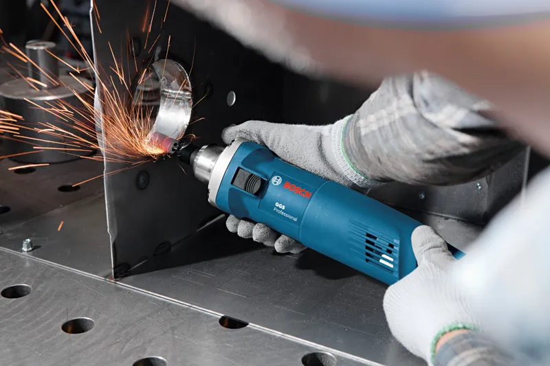 一名佩戴安全设备的人用电动工具研磨金属边缘，产生火花。.