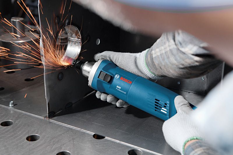 一名佩戴安全设备的人用电动工具研磨金属边缘，产生火花。.