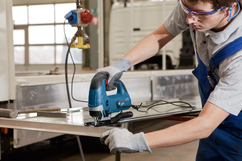 一名佩戴安全设备的人使用曲线锯切割金属板。.