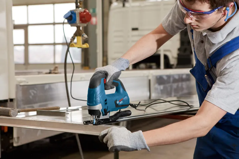 一名佩戴安全设备的人使用曲线锯切割金属板。.