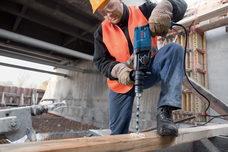一名佩戴安全设备的人员用旋转锤在木梁上钻孔。.